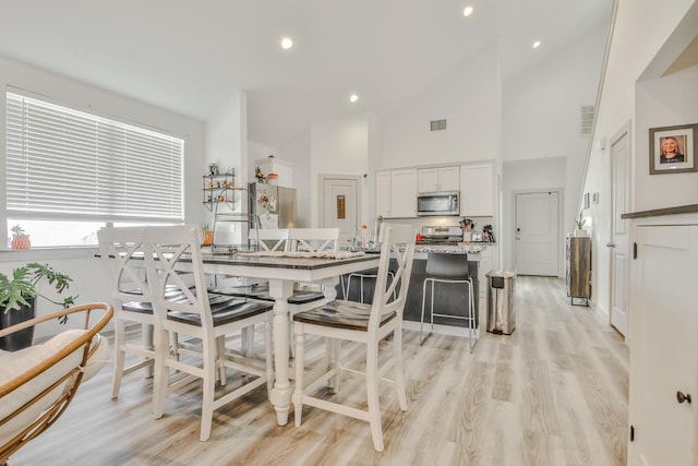 dining area featuring high vaulted ceiling and light hardwood / wood-style flooring