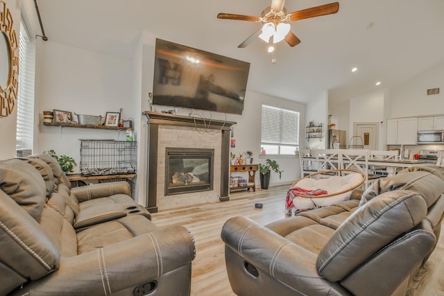 living room with sink, high vaulted ceiling, light hardwood / wood-style flooring, ceiling fan, and a tiled fireplace