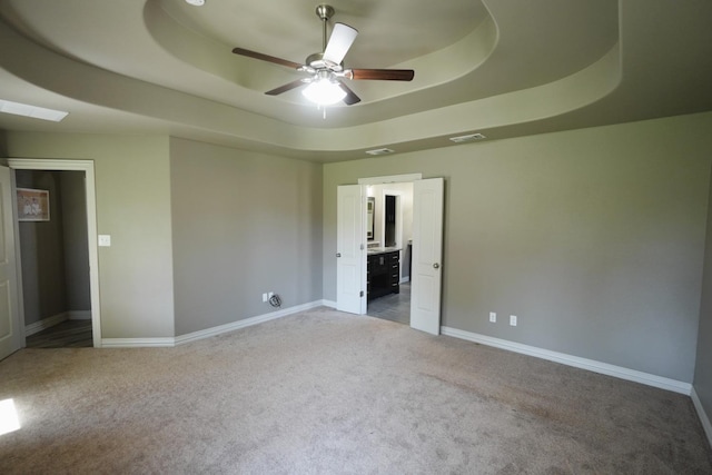 unfurnished bedroom featuring light colored carpet, a raised ceiling, ceiling fan, and ensuite bathroom