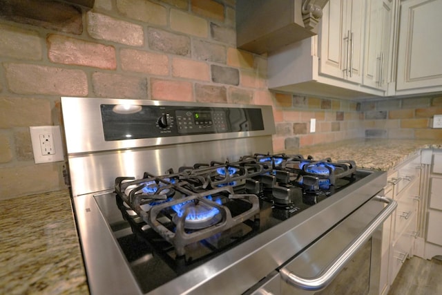 details with gas range, tasteful backsplash, and light stone counters