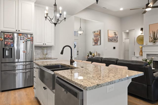 kitchen featuring appliances with stainless steel finishes, a kitchen island with sink, pendant lighting, and white cabinets