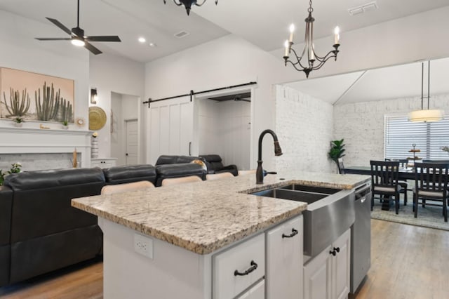 kitchen featuring white cabinetry, hanging light fixtures, stainless steel dishwasher, an island with sink, and a barn door