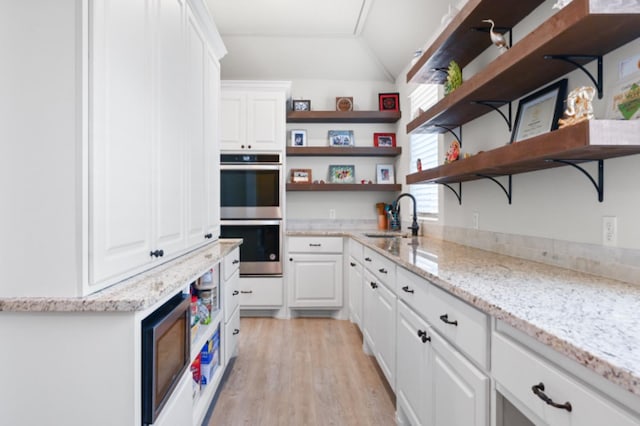 kitchen with sink, white cabinetry, light wood-type flooring, stainless steel double oven, and light stone countertops