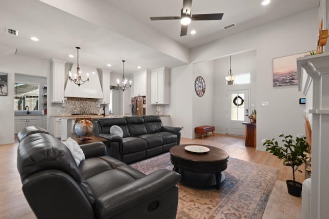 living room featuring ceiling fan with notable chandelier, sink, and light hardwood / wood-style floors