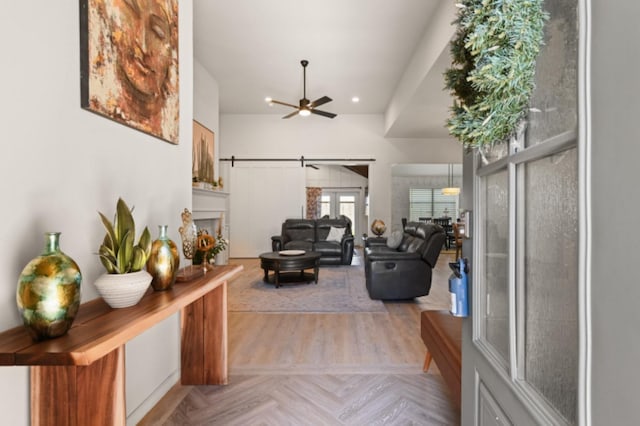 living room featuring ceiling fan, a barn door, and light parquet floors