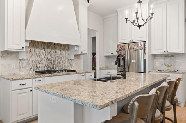 kitchen featuring premium range hood, appliances with stainless steel finishes, white cabinetry, sink, and light stone countertops