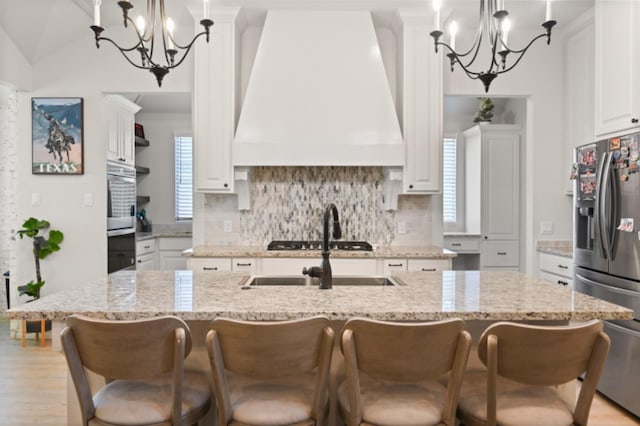 kitchen featuring a notable chandelier, custom exhaust hood, an island with sink, and stainless steel refrigerator with ice dispenser