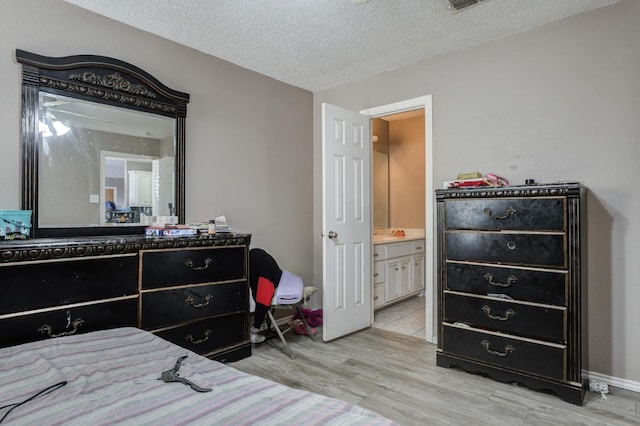 bedroom featuring ensuite bathroom, a textured ceiling, and light wood-type flooring