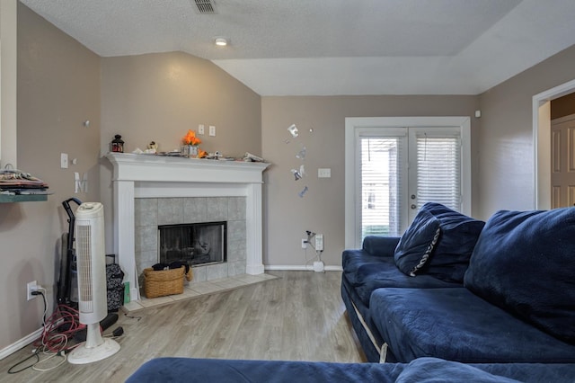 living room featuring vaulted ceiling, a fireplace, hardwood / wood-style flooring, a textured ceiling, and french doors