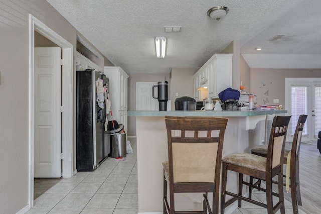 kitchen with kitchen peninsula, stainless steel fridge, a breakfast bar, and white cabinets