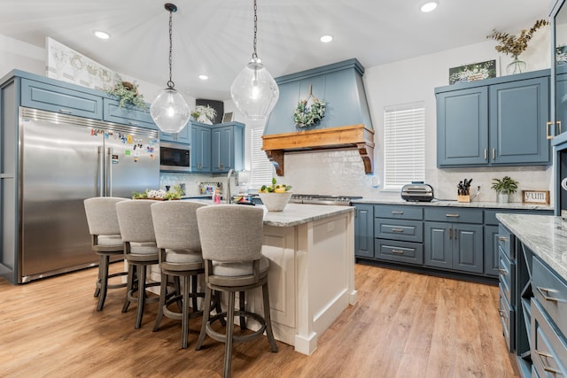 kitchen featuring a center island, blue cabinets, light stone countertops, built in appliances, and custom exhaust hood