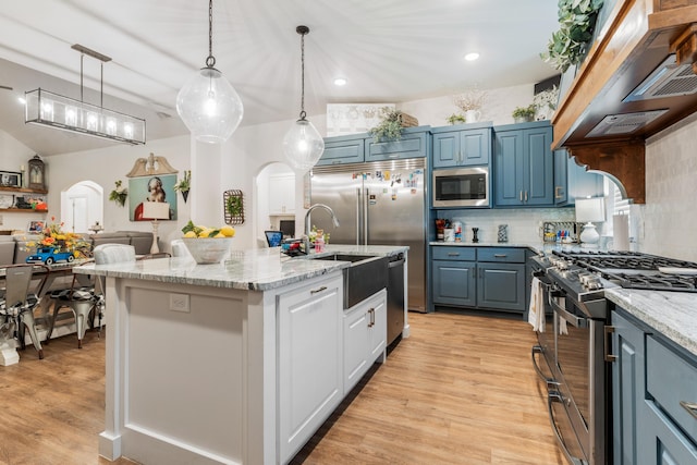 kitchen with arched walkways, stainless steel appliances, custom range hood, hanging light fixtures, and a kitchen island with sink