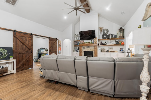 living room with arched walkways, beam ceiling, light wood finished floors, visible vents, and a barn door