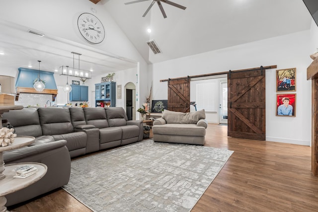 living area with arched walkways, high vaulted ceiling, a barn door, wood finished floors, and visible vents