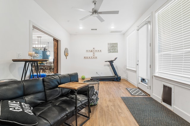 living room with ceiling fan with notable chandelier, light wood-style flooring, visible vents, and baseboards