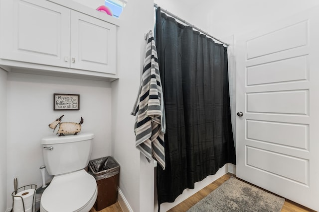 bathroom with toilet, curtained shower, baseboards, and wood finished floors