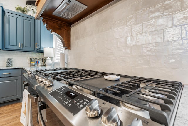 kitchen with tasteful backsplash, stainless steel range with gas cooktop, light wood-type flooring, and light stone counters