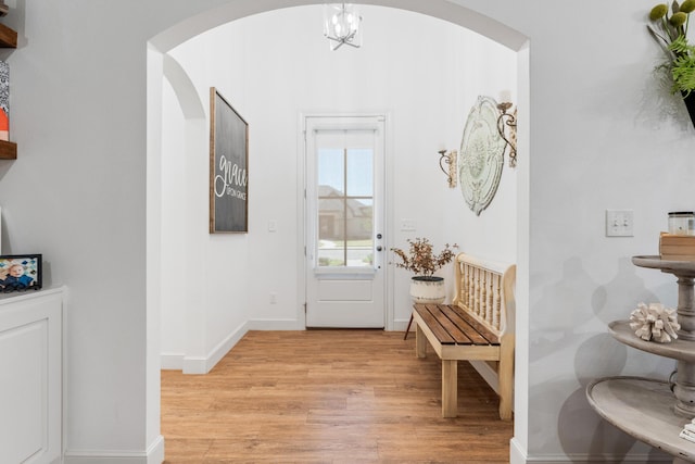 interior space featuring a chandelier, arched walkways, light wood-style flooring, and baseboards