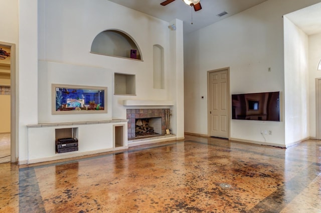 unfurnished living room with a tile fireplace, ceiling fan, and a high ceiling