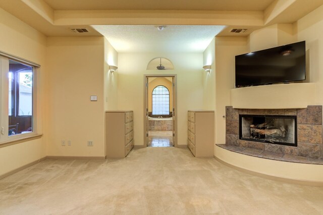 unfurnished living room with a tiled fireplace, carpet, a wealth of natural light, and a tray ceiling