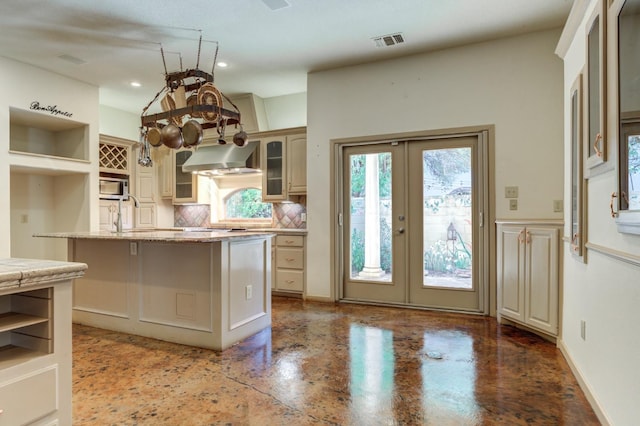 kitchen featuring wall chimney range hood, backsplash, a center island, cream cabinets, and french doors