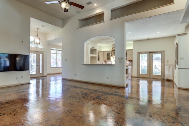 unfurnished living room featuring a towering ceiling, plenty of natural light, french doors, and ceiling fan