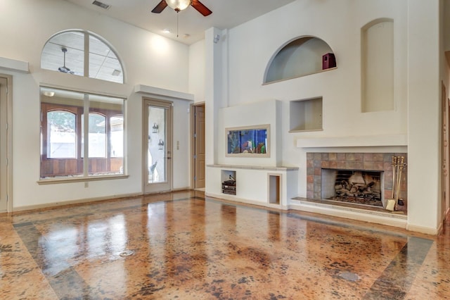 unfurnished living room with ceiling fan, a fireplace, and a high ceiling