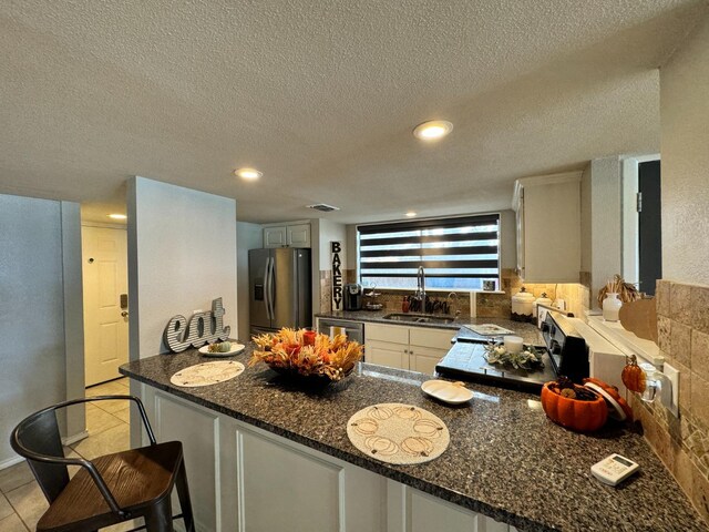 kitchen with sink, white cabinetry, dark stone counters, kitchen peninsula, and stainless steel appliances