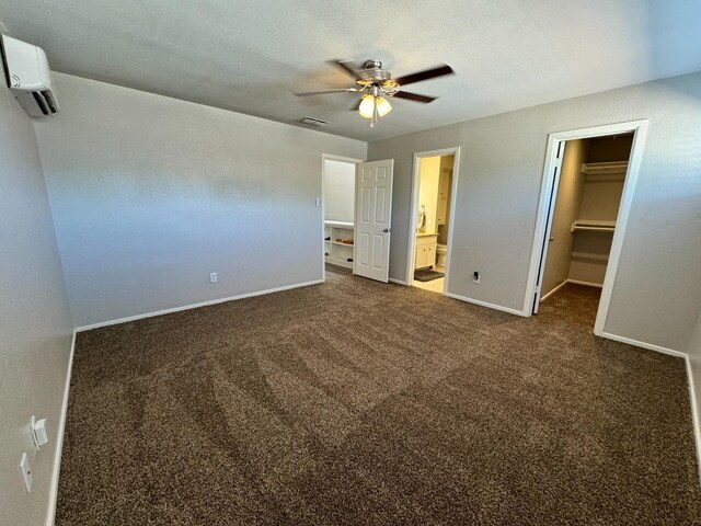 unfurnished bedroom with connected bathroom, dark colored carpet, a walk in closet, ceiling fan, and a closet