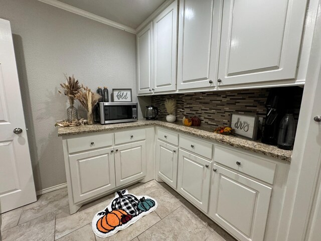 kitchen with tasteful backsplash, white cabinetry, ornamental molding, and light stone counters