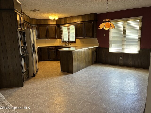 1423 Cherry Blossom Dr, Littlefield, TX 79339 - kitchen with a textured ceiling, a wainscoted wall, a peninsula, high end fridge, and black oven