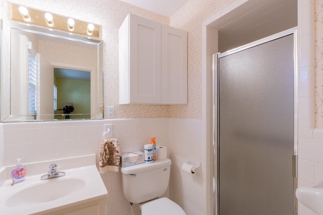 bathroom with vanity, toilet, a shower with door, and tile walls