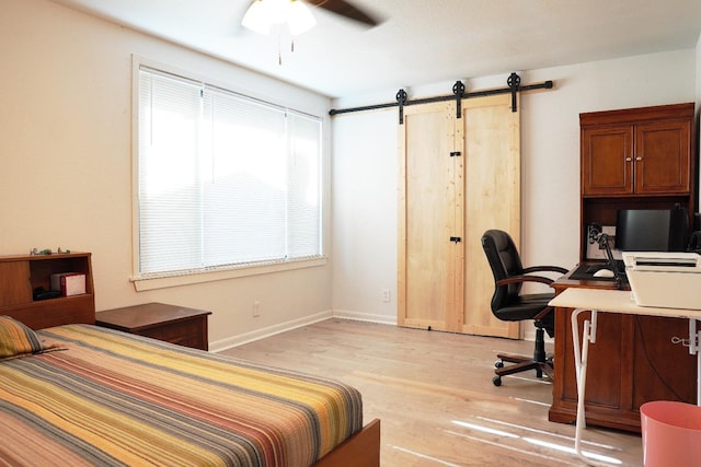 bedroom with a barn door, ceiling fan, and light hardwood / wood-style flooring