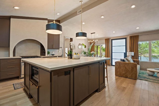 kitchen with light wood-style flooring, light countertops, a center island with sink, and a healthy amount of sunlight