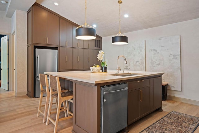 kitchen with freestanding refrigerator, light wood-type flooring, visible vents, a kitchen island with sink, and a sink
