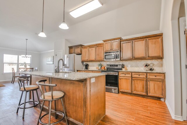 kitchen featuring a breakfast bar area, stainless steel appliances, tasteful backsplash, a center island with sink, and decorative light fixtures