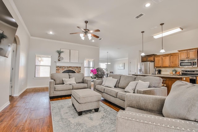 living room with crown molding, ceiling fan, a fireplace, and light hardwood / wood-style floors