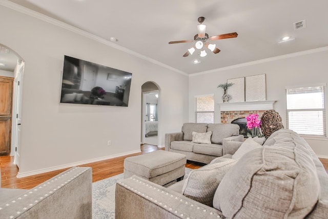 living room with crown molding, ceiling fan, a brick fireplace, and light wood-type flooring