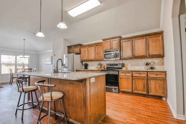 kitchen with appliances with stainless steel finishes, a breakfast bar, a center island with sink, and decorative light fixtures