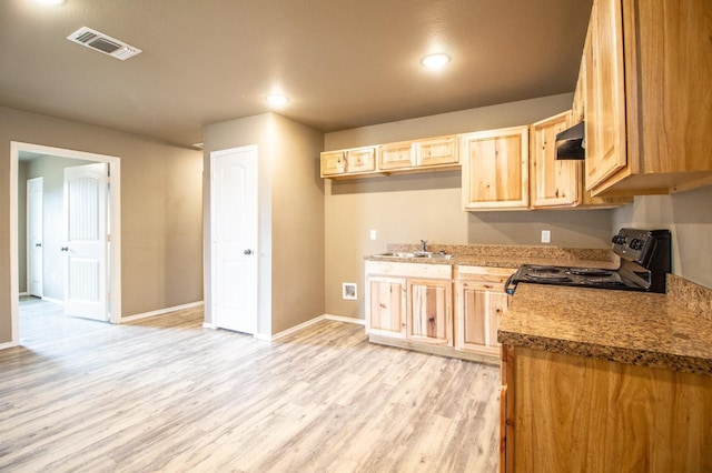 kitchen with sink, dark stone countertops, range with electric cooktop, light brown cabinetry, and light wood-type flooring