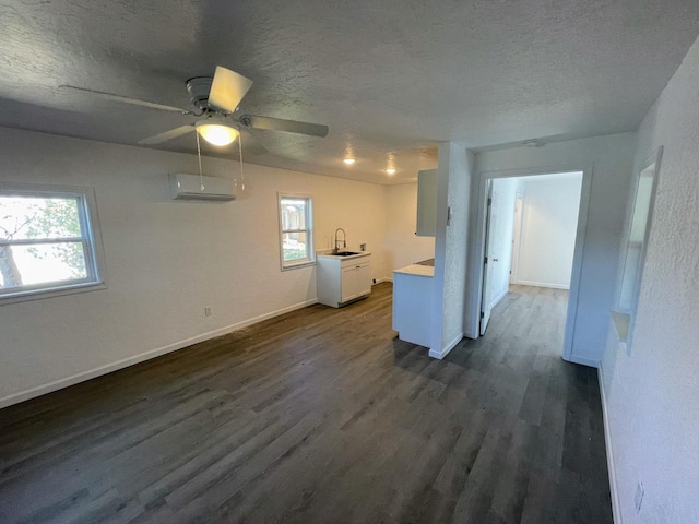 unfurnished living room with sink, a textured ceiling, dark hardwood / wood-style floors, a wall unit AC, and ceiling fan