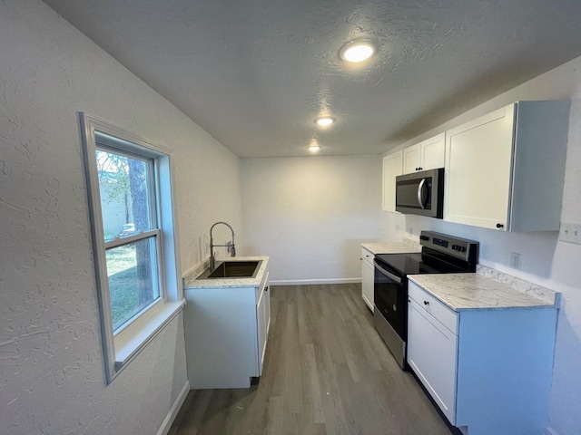 kitchen featuring appliances with stainless steel finishes, wood-type flooring, sink, white cabinets, and a textured ceiling