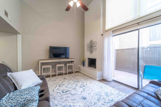 living room featuring ceiling fan, a large fireplace, light hardwood / wood-style floors, and a high ceiling