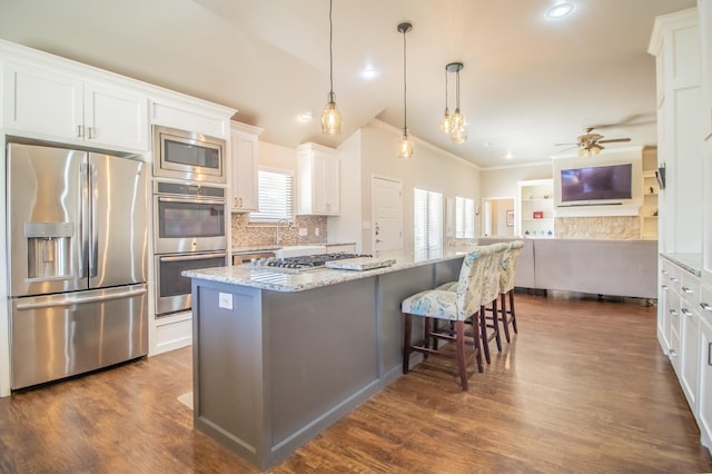 kitchen featuring a center island, appliances with stainless steel finishes, a kitchen breakfast bar, light stone countertops, and white cabinets