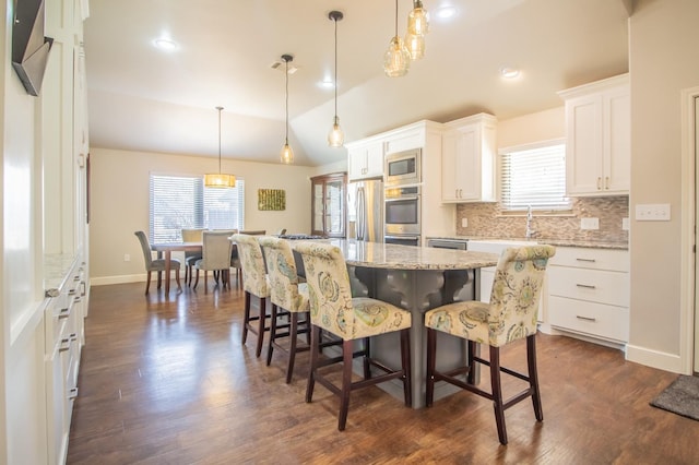 kitchen with pendant lighting, appliances with stainless steel finishes, white cabinetry, a kitchen island, and vaulted ceiling