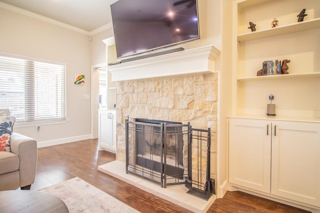 living room with crown molding, wood-type flooring, a stone fireplace, and built in shelves