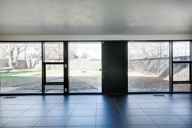 doorway to outside featuring tile patterned floors, a healthy amount of sunlight, and a textured ceiling