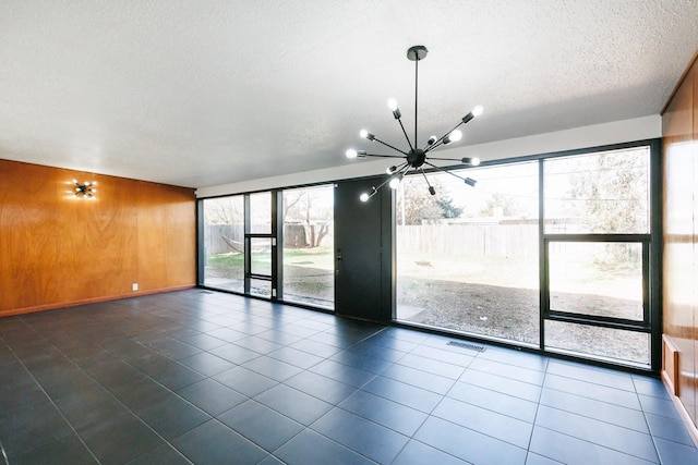 empty room featuring dark tile patterned floors, a textured ceiling, an inviting chandelier, and wood walls