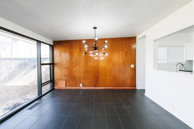 interior space with a notable chandelier, sink, a textured ceiling, and wood walls