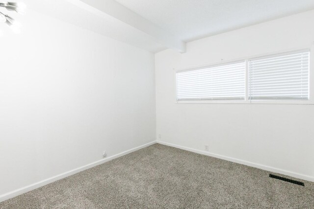 unfurnished room with beamed ceiling and carpet